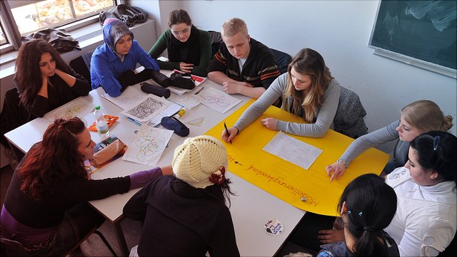 Eine Gruppe von Studierenden sitzen an einem Tisch und erstellen ein Plakat