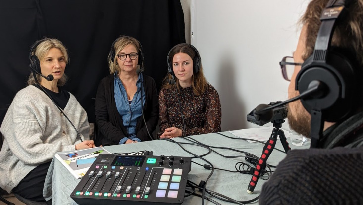Drei Personen sitzen mit Kopfhörern im Aufnahme-Studio.
