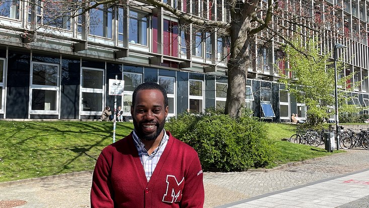Dr Julius Hanks in red sweatshirt in front of the faculty building in spring
