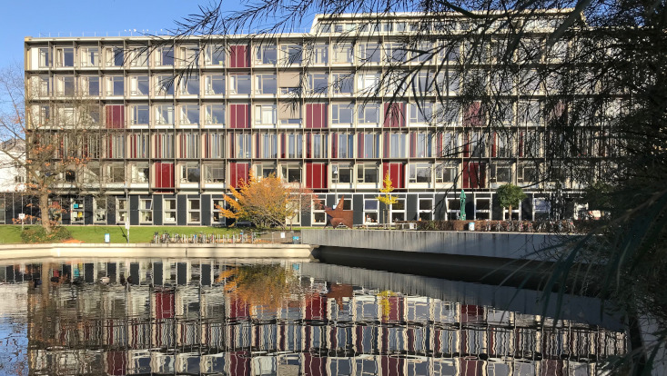 Die Fassade der Fakultät für Erziehungswissenschaft spiegelt sich im Ententeich im Vordergrund.