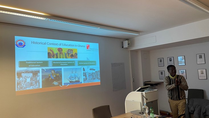 Prof Dampson steht seitlich vor einer Präsentation über Ghana in einem Seminarraum