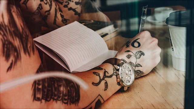 Tätowierter Arm mit Uhr schreibt in Notizbuch