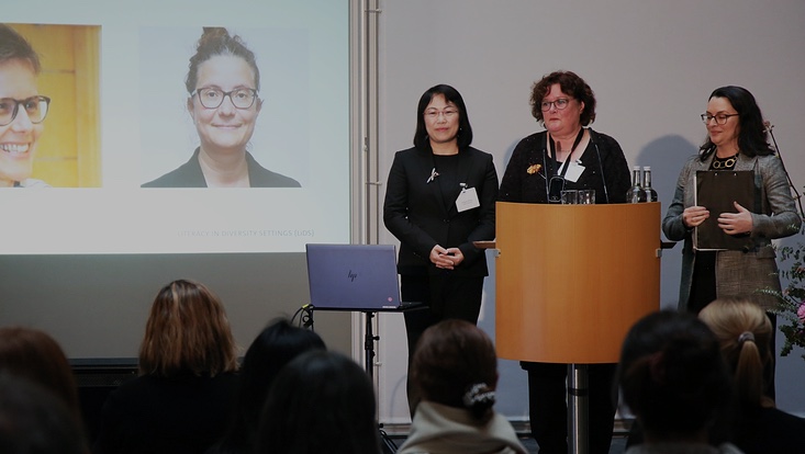 3-733x414 Blick auf die Bühne. Drei Frauen vor Sprechpult. Präsentation daneben.