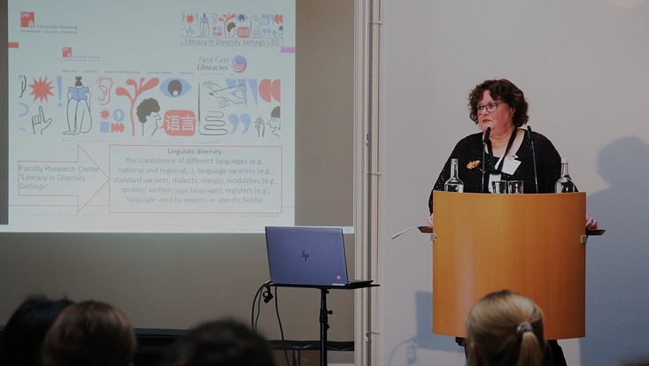 6-733x414 Blick auf die Bühne. Frau vor Sprecherpult. Präsentation daneben.