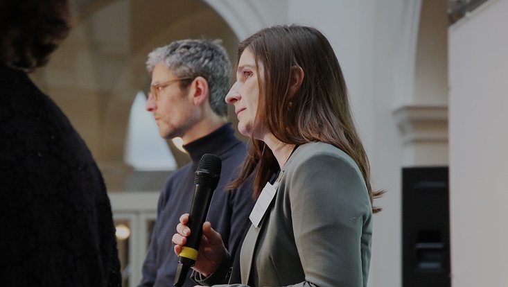 7-733x414 Seitliche Nahaufnahme. Frau mit Mikrofon. Mann im Hintergrund.