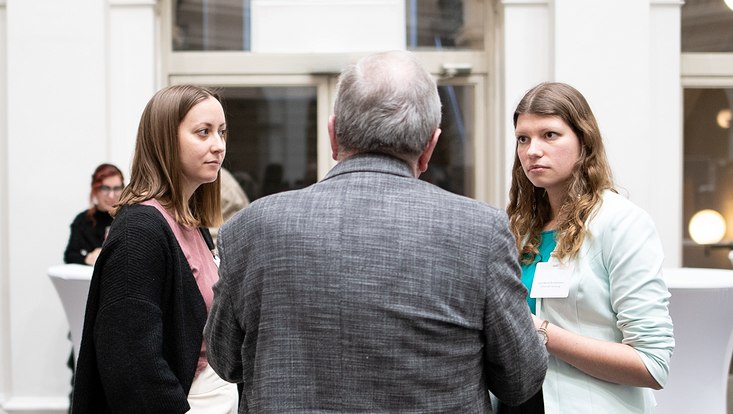 15-733x414 Blick auf den Rücken einer Mann, welche im Gespräch mit zwei Frau ist.