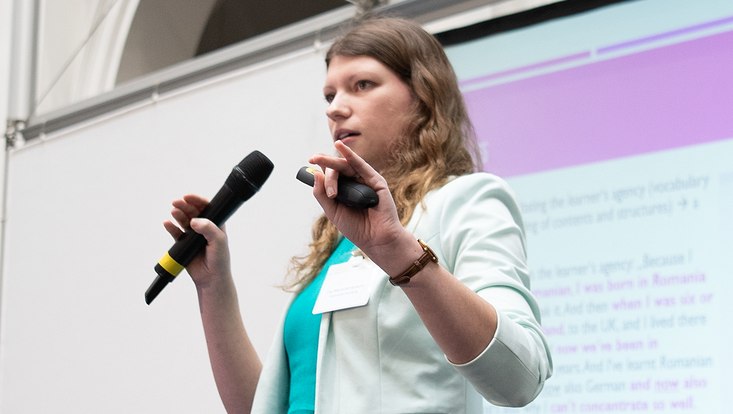 16-733x414 Blick von unten auf eine Frau mit Mikrofon in der Hand.