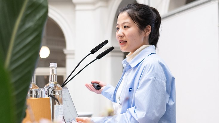 17-733x414 Frau auf Bühne vor Mikrofon.