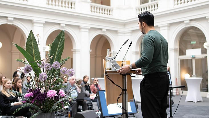 18-733x414 Mann auf Bühne von hinten. Publikum im Hintergrund.