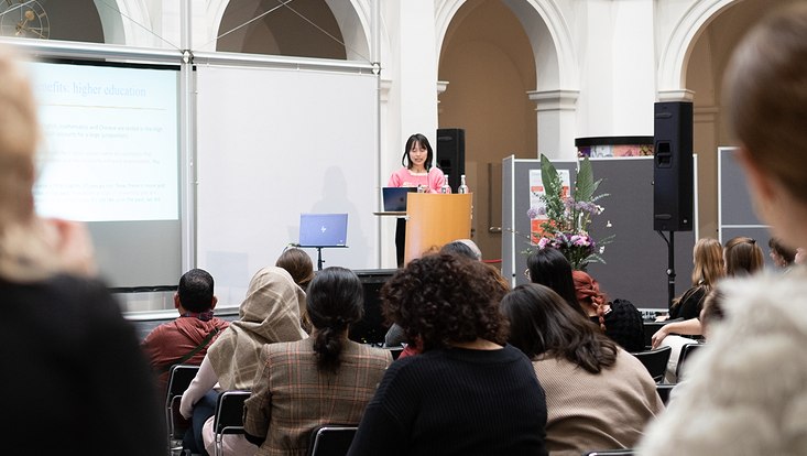 19-733x414 Blick aus dem Publikum auf die Bühne. Frau spricht auf Bühne.
