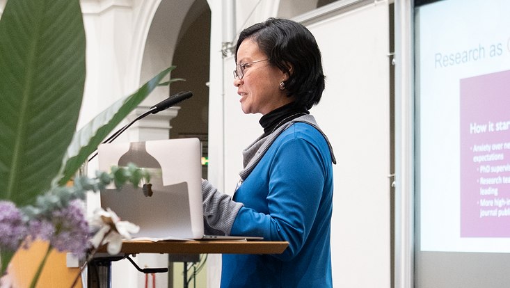 27-733x414 Seitlicher Blick auf Sprecherin auf Bühne. Präsentation im Hintergrund.