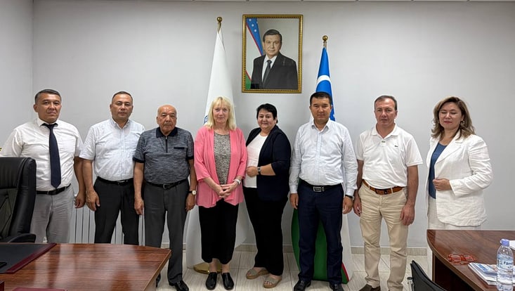 Telse Iwers, Dilbar Ernazarova und mehrere Teilnehmende des Treffens an der Uni für Pädagogik und Wirtschaft stehen in einer Reihe. Hinter ihnen an der Wand stehen usbekische Flaggen und ein Porträt des Usbekischen Staatsoberhauptes hängt an der Wand