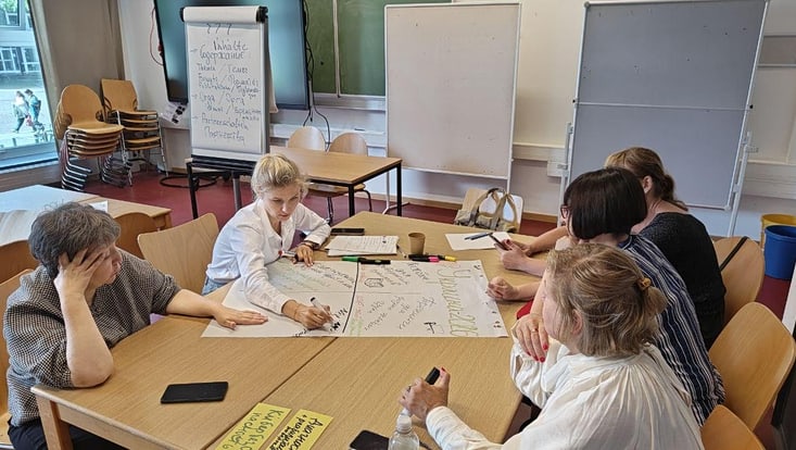 2-733x414 Teilnehmende arbeiten in Gruppen an einem Tisch im Seminarraum