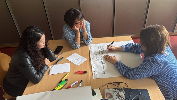 3-733x414 Teilnehmende arbeiten in Gruppen an einem Tisch im Seminarraum