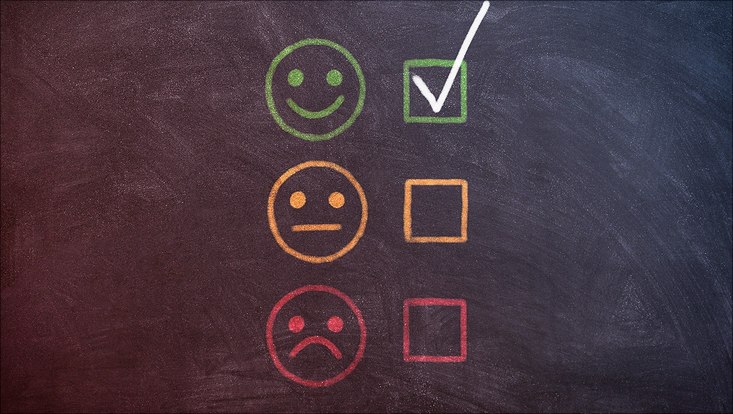 Drei Smileys (lachend, gleichgültig, unglücklich) mit Kästchen zum Markieren in grün, geld und rot auf dunkler Tafel