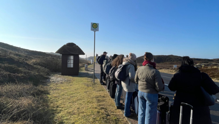 Studierende auf Lernreise. Personen warten auf den Bus.