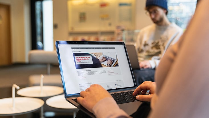Zu sehen ist eine Person mit einem Laptop auf dem Schoß. Die Kamra blickt von hinten, der Laptop ist zentral im Bild positioniert