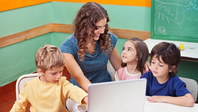 Lehrkräfte Grundschullehrkraft schaut mit Kindern auf ein Notebook.