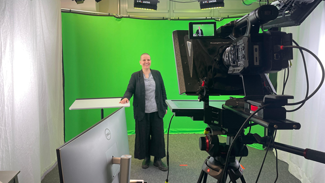 Forscher*in steht im Videostudio vor einem Greenscreen mit Kameras und Beleuchtung im Bild