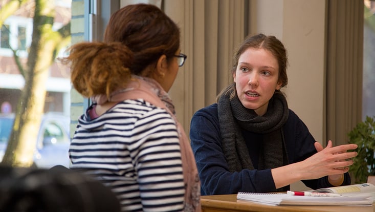 Zwei Studentinnen sitzen im Foyer von VMP8 und unterhalten sich.