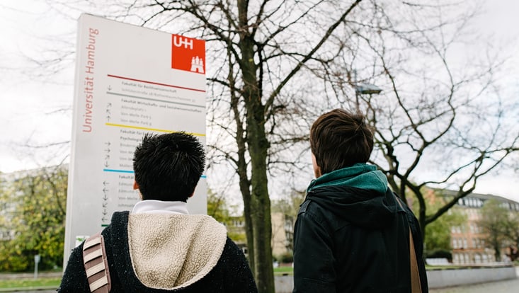 Junge Menschen schauen auf einen Wegweiser auf dem Campus