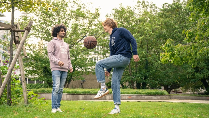Zwei Studierende spielen auf einer Wiese mit einem Basketball.