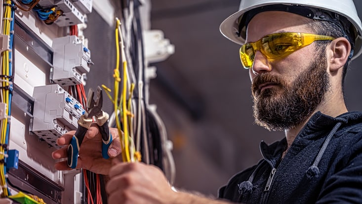 Elektriker an Maschine mit Zange an Kabel