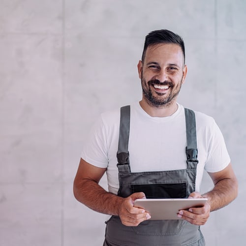Junger männlicher Arbeiter in einer Gesamtuniform mit Tablet an seinem Arbeitsplatz.