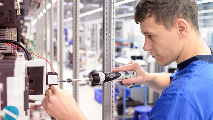 Junger Lehrling in einem Industrieunternehmen, das elektronische Bauteile im Maschinenbau einer modernen Fabrik montiert