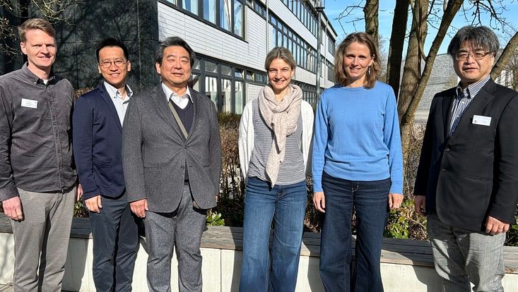 Gruppenbild des Schulleiters der STS Bergedorf, der japanischen Gastwissenschaftler, einer Mitarbeiterin der UHH und der Didaktischen Leitung der STS Bergedorf draußen vor der Schule in der Sonne.