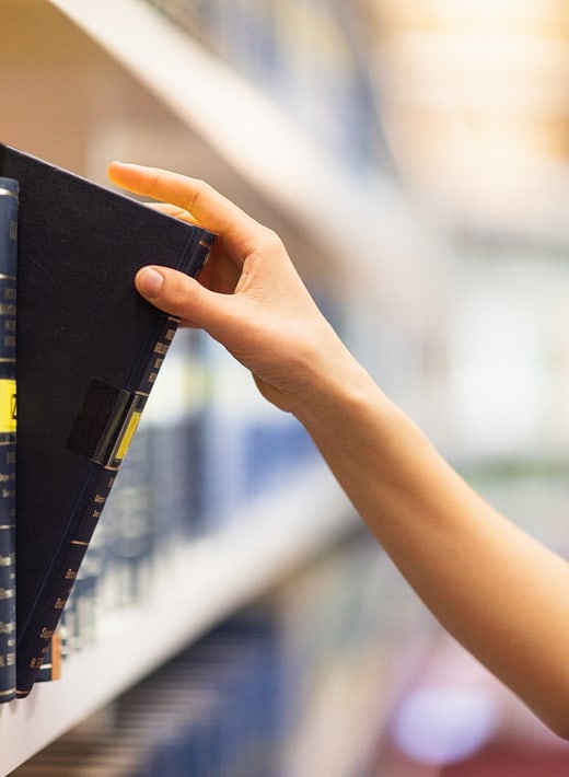 Person greift nach Buch im Regal