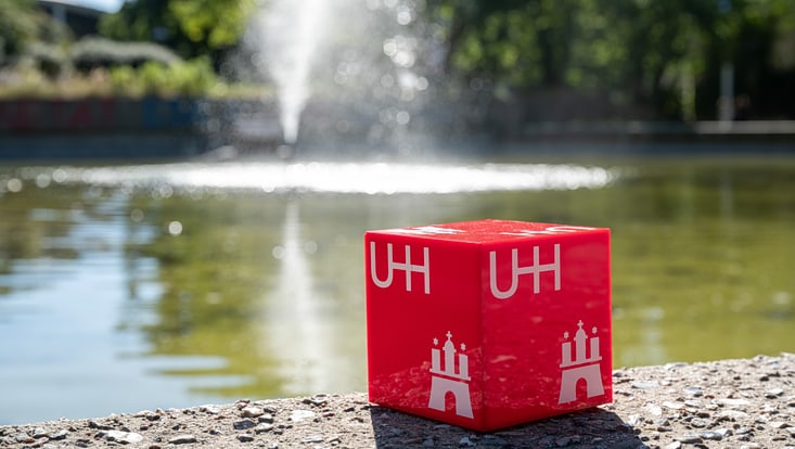 Ein roter Plastikwürfel mit dem UHH-Logo steht auf der Betonumrandung des Ententeichs am Von-Melle-Park.