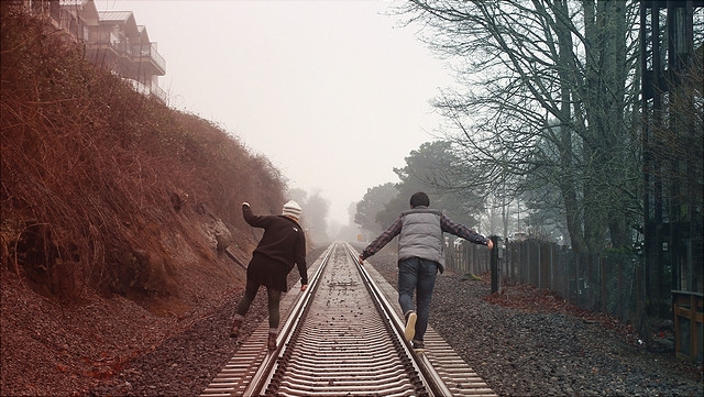 Zwei Jugendliche laufen auf Schienen in den Nebel.