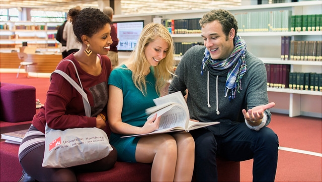 Studierende in Bibliothek sprechen über ein Buch.