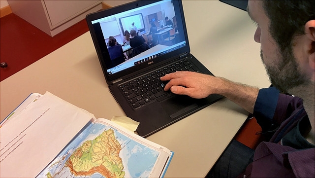 Mann an Laptop mit Atlas daneben