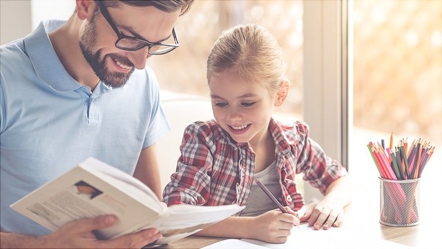 Vater schaut sich mit Tochter Schulbuch an.
