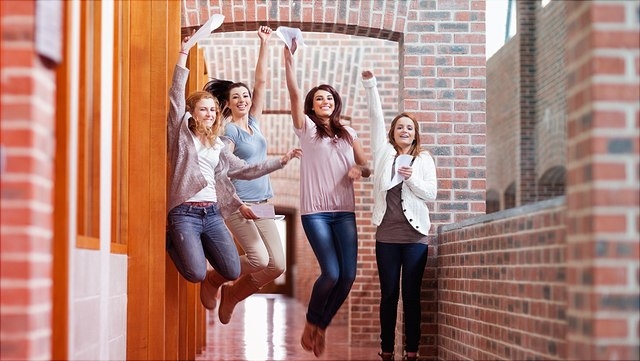 Ältere Schüler springen in die Luft mit Zeugnissen in der Hand.