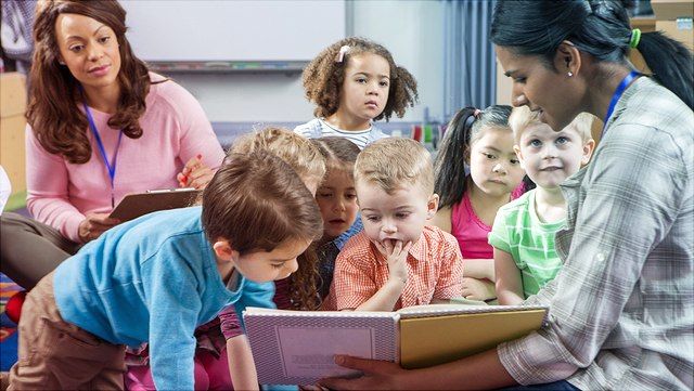 Kinder verschiedener Ethnien hören Erzieherin im Kindergarten zu.