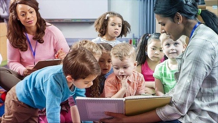 Kinder verschiedener Ethnien hören Erzieherin im Kindergarten zu.