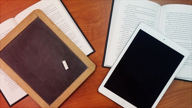 Tafel mit Stück Kreide auf Buch, Tablet auf Buch