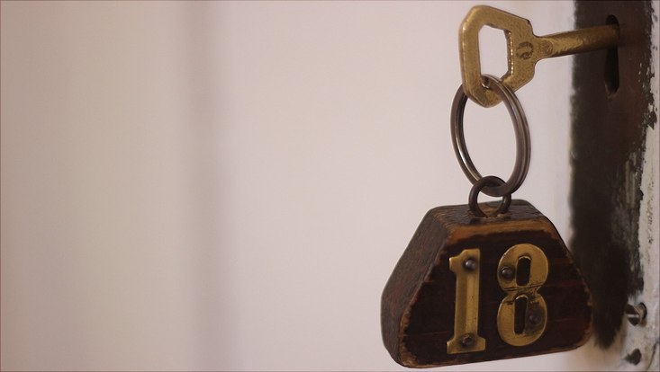 Ein altmodischer Schlüssel steckt in einem Türschloss, auf dem hölzernen Schlüsselanhänger steht die Zahl 18