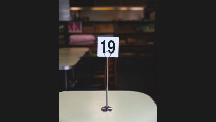 Auf einem Tisch steht ein Kärtchenhalter mit eingestecktem Kärtchen, auf diesem steht die Zahl 19