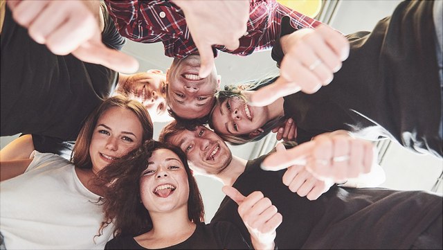 Buddy Programm Eine Gruppe steht lachend im Kreis, den Blick nach unten in die Kamera gesenkt