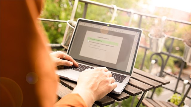 Eine Person arbeitet Eine Person arbeitet mit Laptop an einem Tisch auf dem Balkon