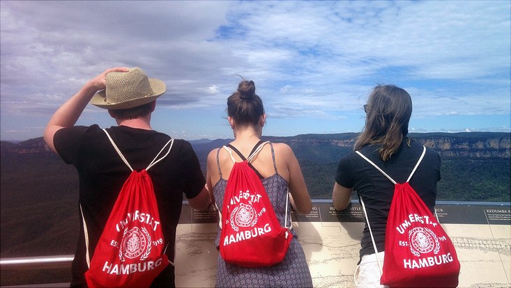 drei Studierende mit roten Turnbeuteln mit UHH-Logo blicken auf Blue Mountains