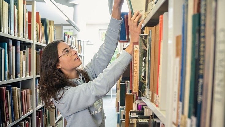 Studentin nimmt Buch aus Regal