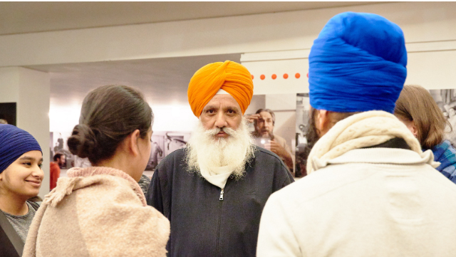 Mehrere Turban tragende Menschen unterhalten sich. Einer von ihnen guckt direkt in die Kamera.