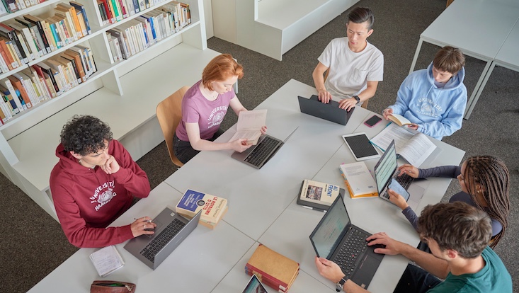 studieren-733-414-von-wieding Vogelperspektive auf einen Tisch, an dem mehrere Studierende an Laptops arbeiten