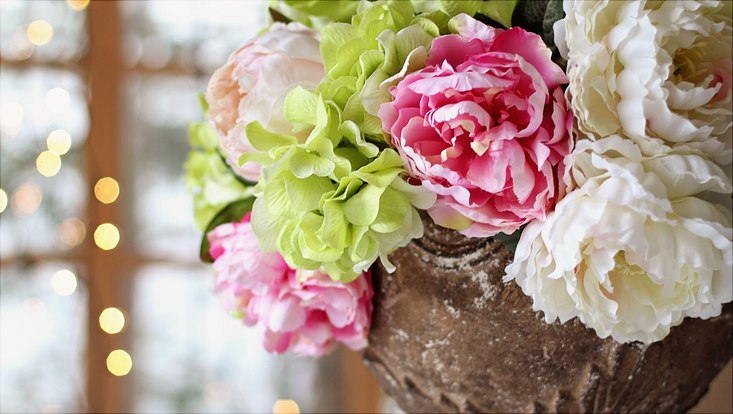 Vase mit rosa und weißen Pfingstrosen und grünen Hortensien vor einem Fenster