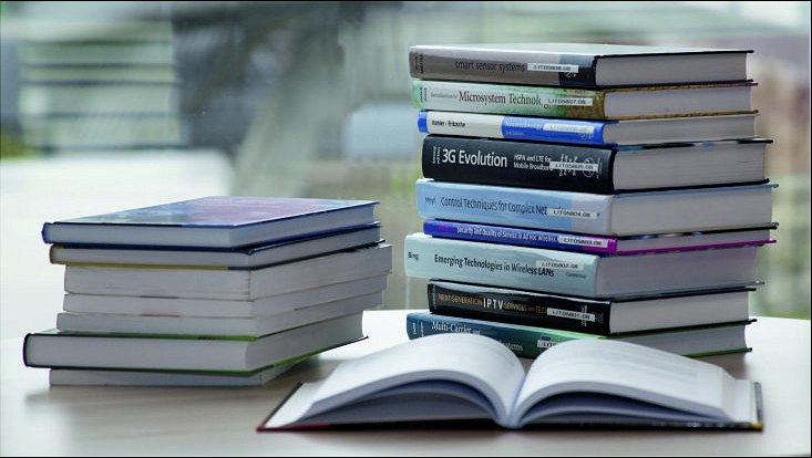 zwei Bücherspapel und ein aufgeschlagenes Buch